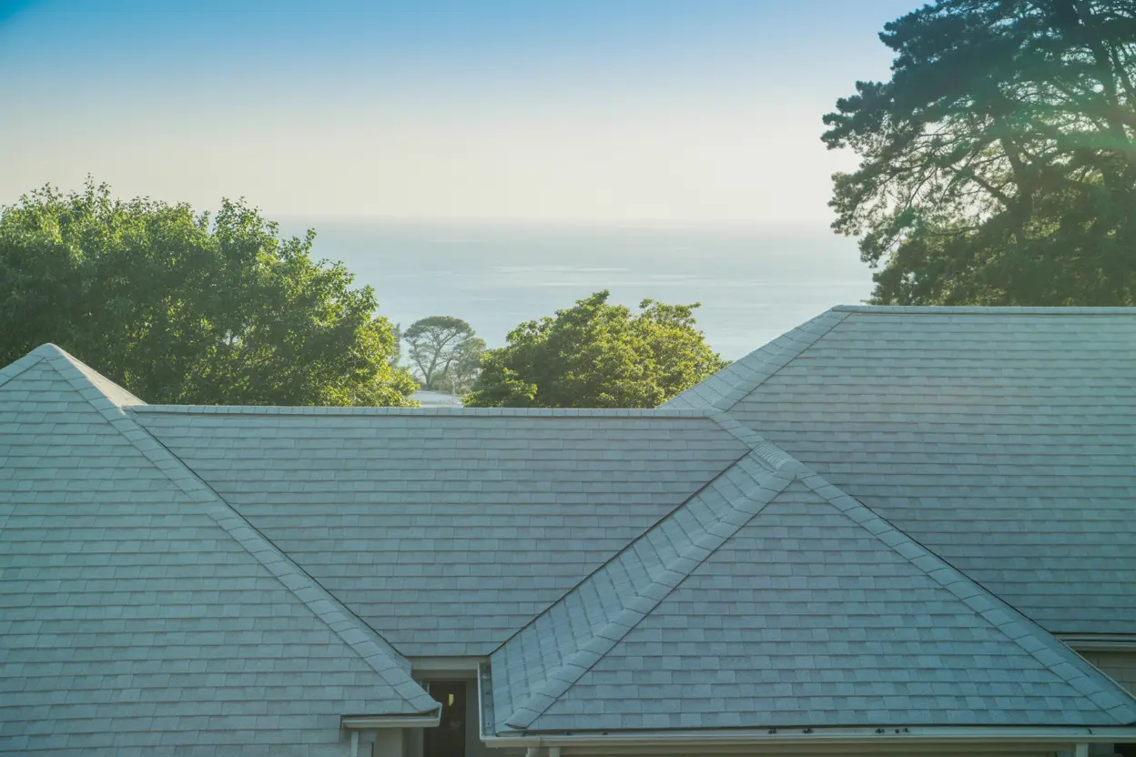 Light-gray hip roof covered in uniform shingles framed by trees with hazy Pacific Ocean backdrop, Lomita.